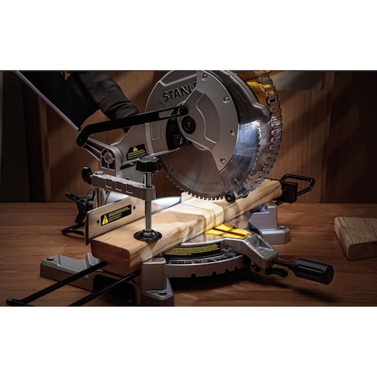STANLEY SM16-B3 miter saw cutting wood, side angle, silver blade, mounted on wooden workbench.