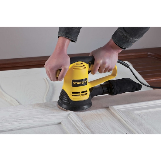 STANLEY SRS480 sander in use on a wooden door, yellow and black design, product photography.