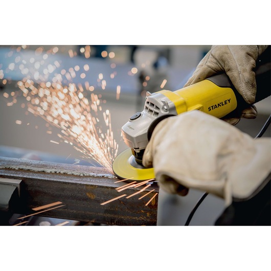 Photo of STANLEY STA0413 angle grinder in use, grinding metal with visible sparks, operated by gloved hands.