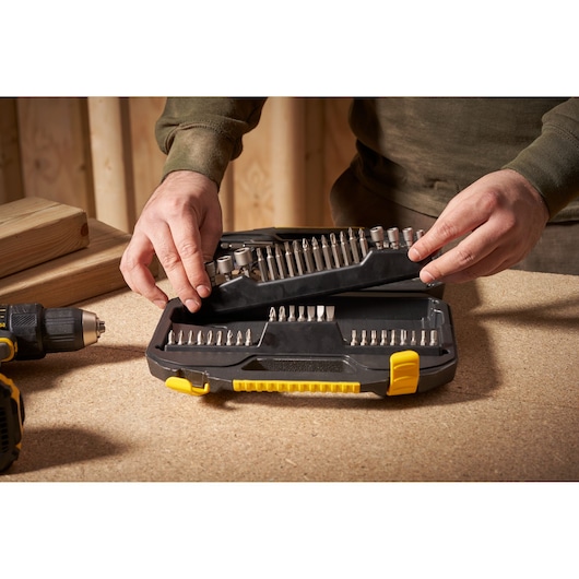 STANLEY STA7184 drill bit set in black and yellow case, open on workbench with person handling.