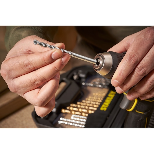 STANLEY STA7184 drill bit set photography, close-up of hand inserting drill bit into power drill.