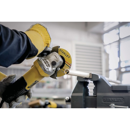 Photo of STANLEY STA8061 angle grinder cutting metal pipe in workshop, gloved hands holding tool.