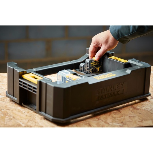 Photo of STANLEY STA88580 tool battery storage box with a hand inserting a battery, shown on a wooden surface.