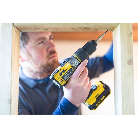 STANLEY STDC18LHBK cordless drill in yellow and black used for construction on wooden frame.