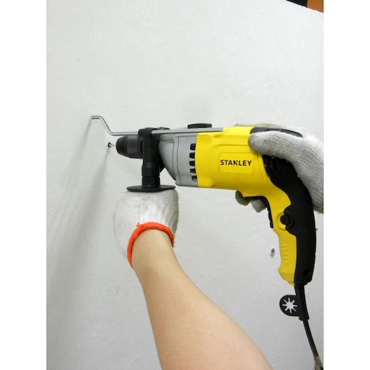 Stanley STDH7213K yellow-black hammer drill used on wall, close side view.