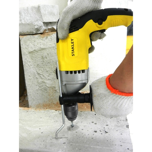 STANLEY STDH7213K yellow and black hammer drill in use drilling concrete, close-up of hands with gloves.