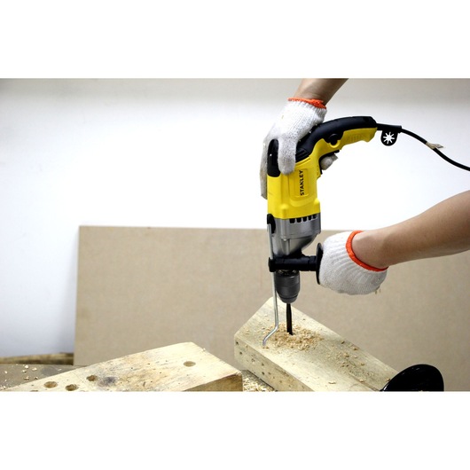 STANLEY STDH7213K drill in use on wood, worker with gloves drilling holes, side view.
