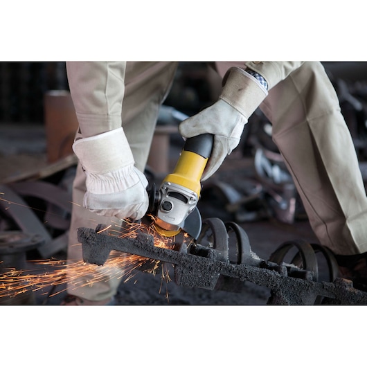 STANLEY STGS7115 angle grinder used on metal part, yellow and black, sparks flying, close-up photo.