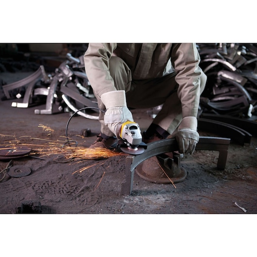 STANLEY STGS7115 angle grinder in use, grinding metal with sparks flying, close-up of tool and worker's hands.