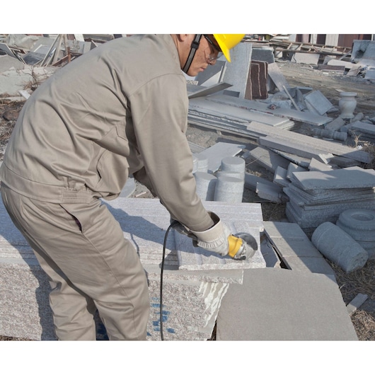 STANLEY STGS7115 angle grinder in use cutting stone, side view, construction worker wearing beige uniform.
