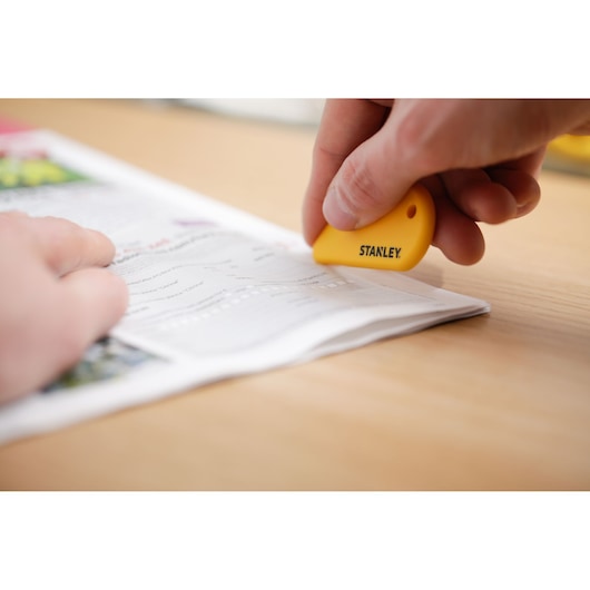 Photo of STANLEY STHT0-10291 yellow safety cutter used to slice paper on a desk.