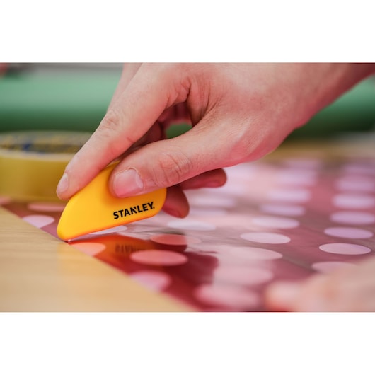 Photo of STANLEY STHT0-10291 compact cutter in hand, cutting red polka dot paper on a table.