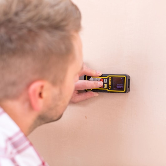 STANLEY STHT1-77138 laser distance measurer in use against a wall, close-up view.