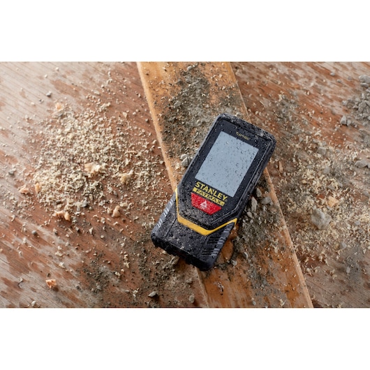 STANLEY STHT1-77139 laser distance measurer on dusty wood surface, rugged design, construction context.