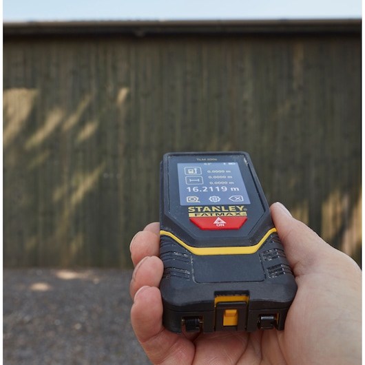 STANLEY STHT1-77140 laser distance measurer in hand, display screen showing measurements, outdoor use.