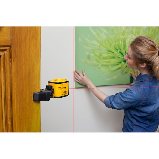 STANLEY STHT1-77340 laser level mounted on a door frame projecting red lines while a person hangs a picture.