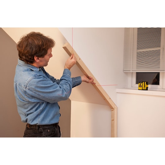 STANLEY STHT1-77341 cross line laser level projecting red lines on wall near window, used for aligning wooden beam.