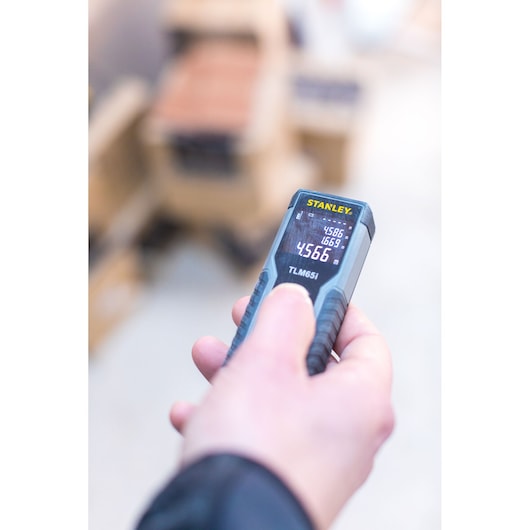 Stanley STHT1-77354 laser distance measurer TLM65i held in hand, display shows measurement value.