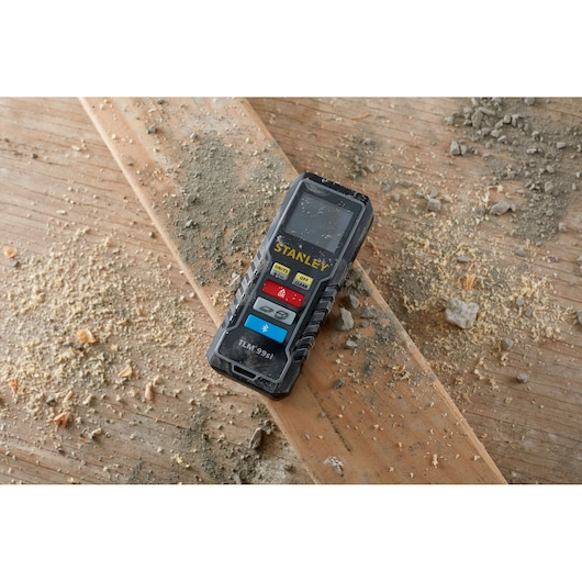 Stanley STHT1-77361 laser distance measurer on dusty wooden board, construction setting.