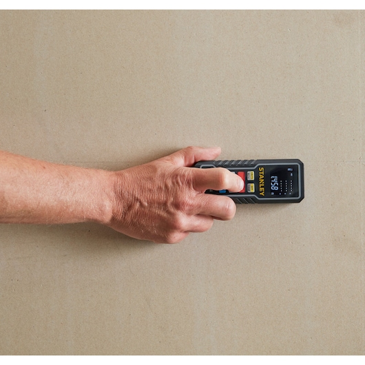 STANLEY STHT1-77361 digital laser distance measurer in hand, measuring on a wall, top view.