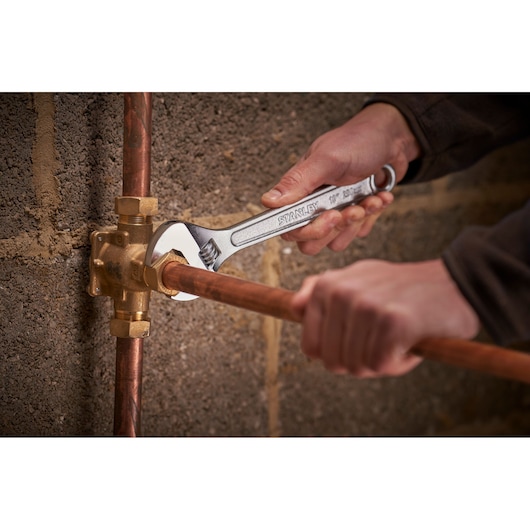 Stanley STHT13121-0 adjustable wrench used on copper plumbing pipe, close-up photography.