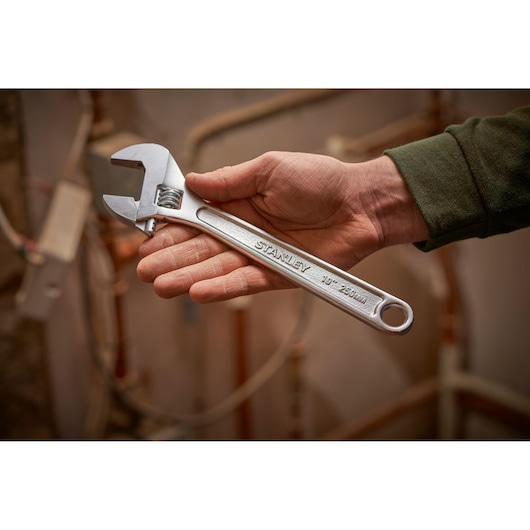 Photo of a hand holding a STANLEY STHT13122-0 adjustable wrench, silver, 250mm, in a workshop setting.