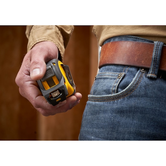 Photo of STANLEY STHT37235 tape measure held in hand near denim jeans and leather belt.
