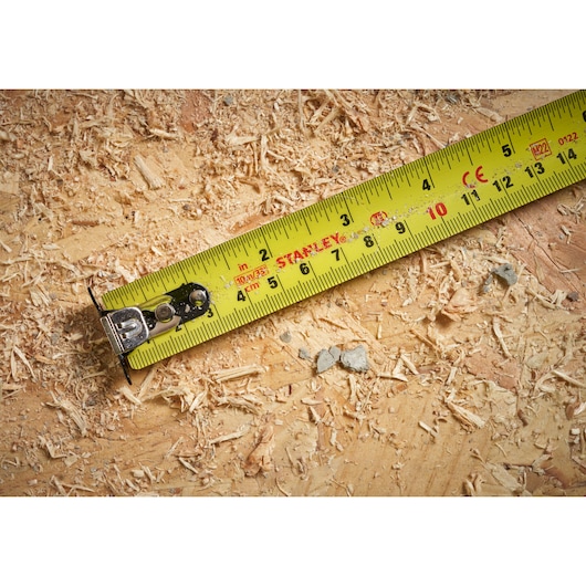Photo of STANLEY STHT37237 yellow tape measure on a wood surface with sawdust.
