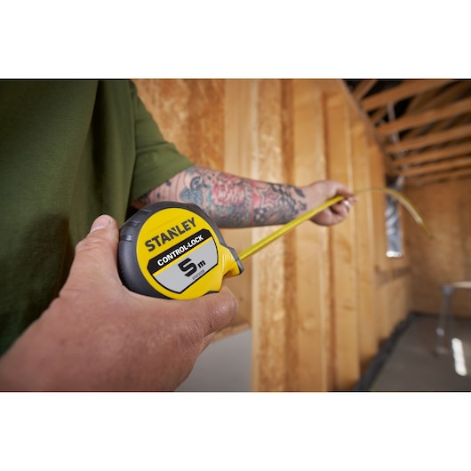 Stanley STHT37239 tape measure being used indoors on a construction site, close-up holding yellow and black tool.