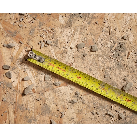 STANLEY STHT37239 tape measure extended on dusty plywood with construction debris.