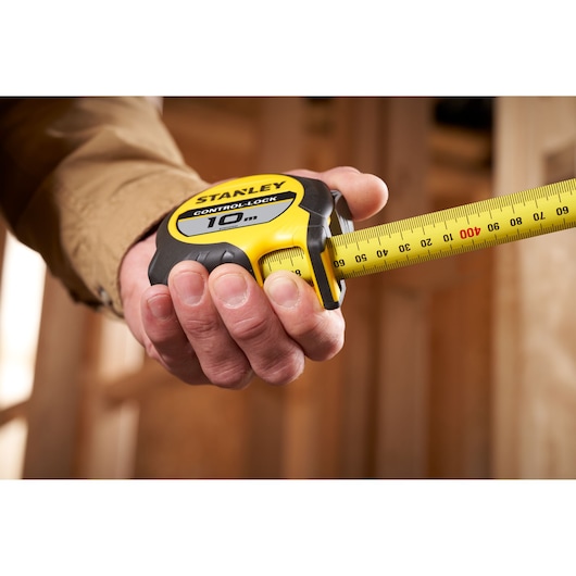 Hand holding a STANLEY 10m tape measure with yellow casing, used for measuring lengths in construction.