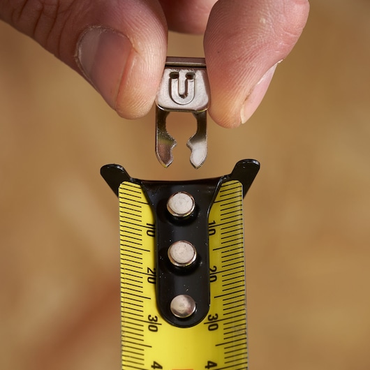 Close-up of a hand attaching a metal accessory to a yellow Stanley tape measure.