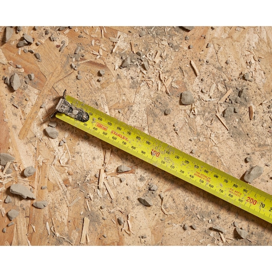 Stanley yellow tape measure on a rough wooden surface with debris and small rocks.