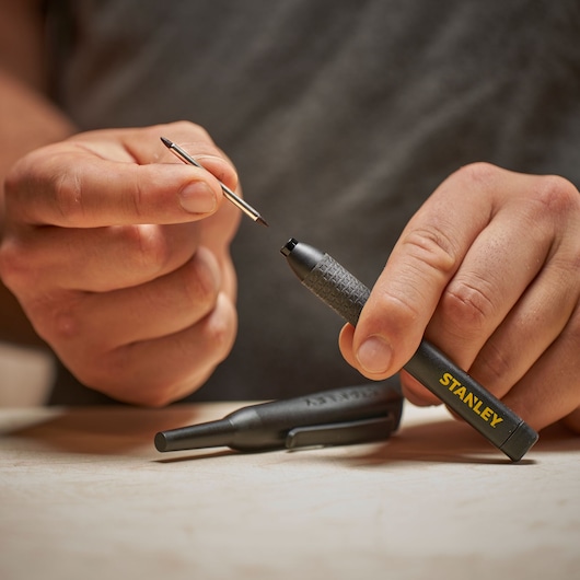 Hand holding a STANLEY pen with its refill being replaced, on a light surface.