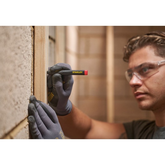 Person marks wood with STANLEY carpenter pencil while wearing gloves and safety glasses.