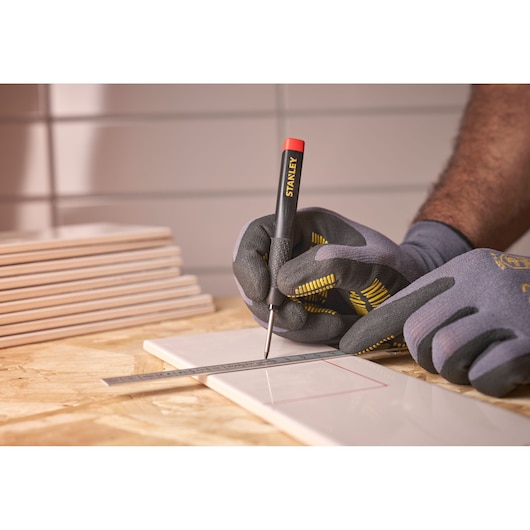 Gloved hands mark a tile with a STANLEY tool and metal ruler on a wooden surface.