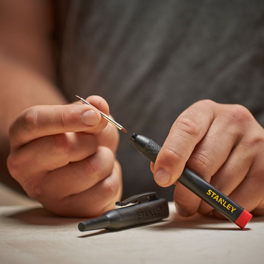 Person holds a STANLEY photo marker and a pin, with the black marker cap placed on a table.