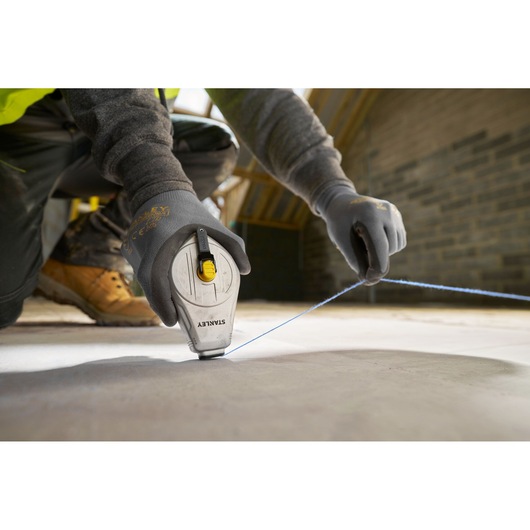 STANLEY STHT47110-0 chalk line being used on a construction site, close-up of hands with gloves pulling blue line.