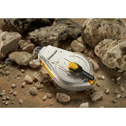 STANLEY STHT47110-0 chalk line reel with silver and yellow body on a dusty surface with rocks, product photography.