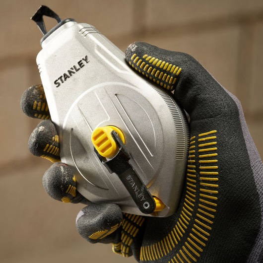 Photo of STANLEY STHT47110-0 chalk line reel, silver body, yellow accents, held in gloved hand.
