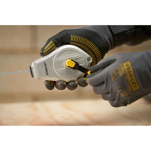 Photo of STANLEY STHT47110-0 chalk line reel being used by gloved hands, close-up view.