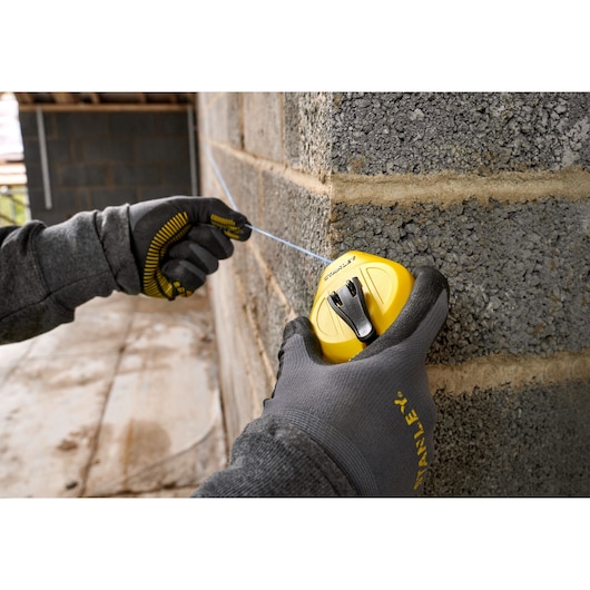 STANLEY STHT47112-0 chalk line reel used on a concrete wall, worker wearing gloves, close-up photography.