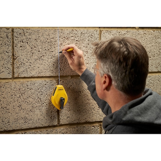 Photo of STANLEY STHT47112-0 chalk line reel marking a straight line on a concrete wall, side view.