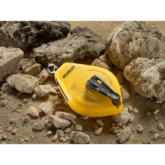 Photo of STANLEY STHT47112-0 chalk line tool in yellow, placed on rocky ground.