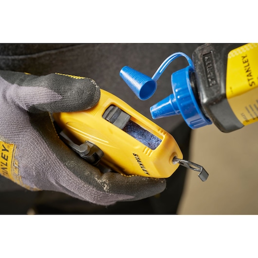 STANLEY STHT47112-0 chalk line reel with blue chalk bottle close-up, held by gloved hand.