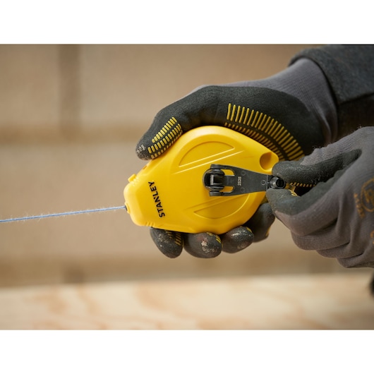 STANLEY STHT47112-0 yellow chalk line reel held in gloved hands, photography category.