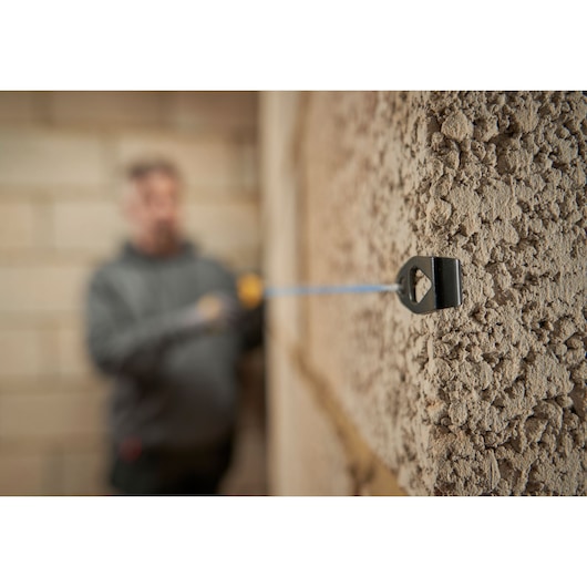 Photo of STANLEY STHT47112-0 tape measure in use on rough wall, close-up of hook attached to concrete surface.
