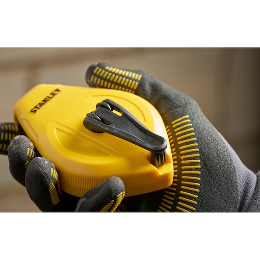 Photo of STANLEY STHT47112-0 yellow chalk line reel held in gloved hand, black clip visible, close-up view.