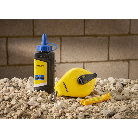 Photo of STANLEY STHT47113-0 chalk line set with yellow reel, chalk bottle, and level on gravel.