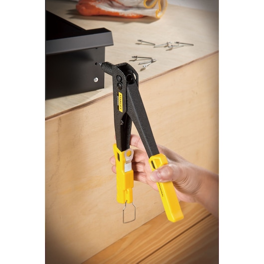 STANLEY STHT69800-8 riveter tool with yellow handles in use, fastening metal to wood, close-up angle.